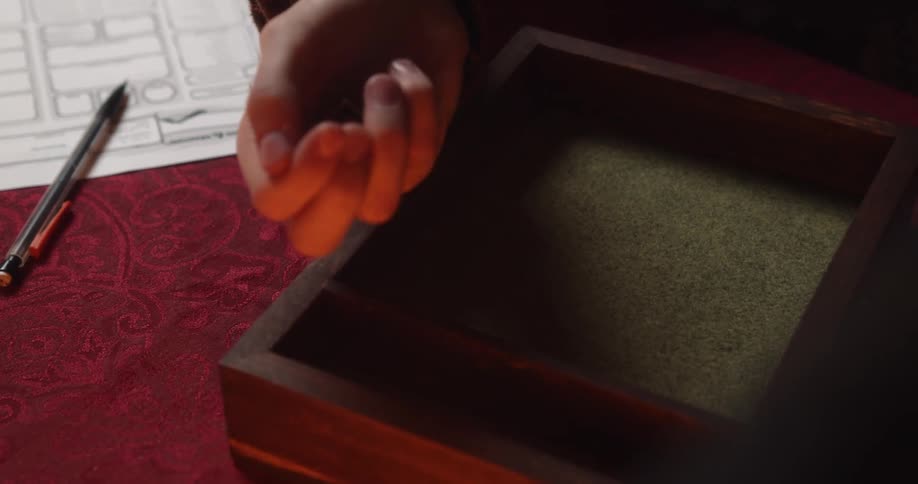 A person tossing four dice into a box on a table with a paper and pen next to them