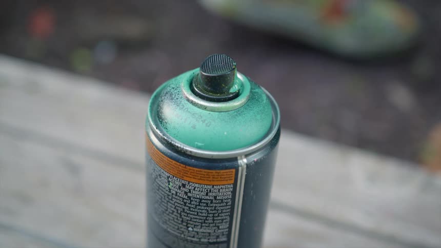 Aerosol paint can sits on wooden table near person wearing colorful shoes