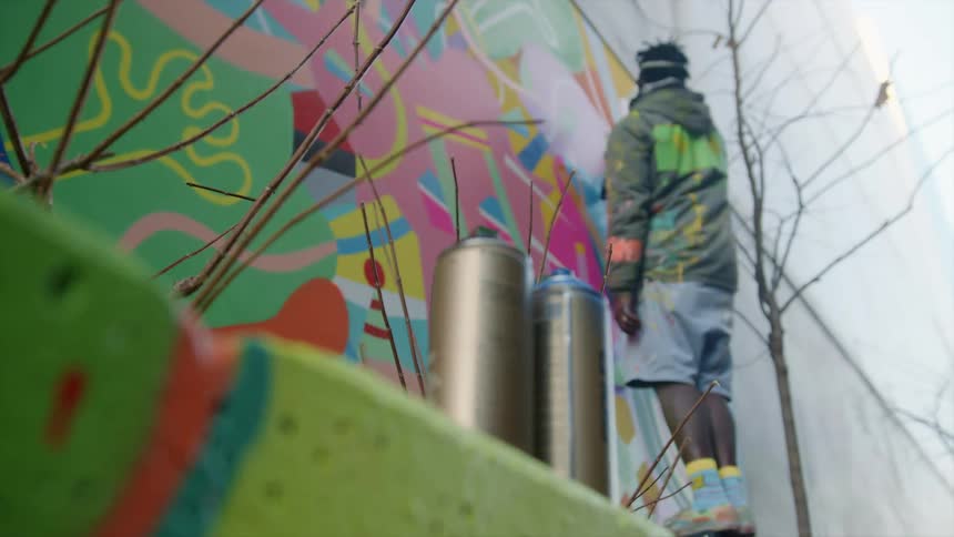 A man painting graffiti on a wall with spray cans in the foreground