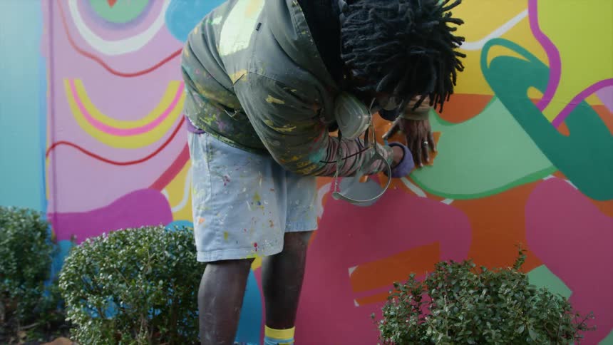 A man painting a mural outdoors marks an area off with tape