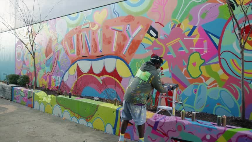 A man with a spray can and a mask and a ladder walking up to a wall with graffiti
