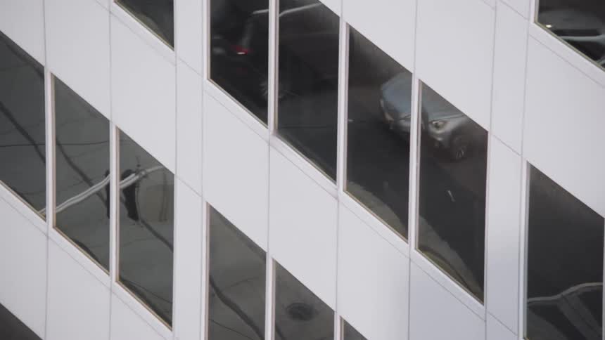 Cars traveling on a city street are reflected on the windows of a building facade