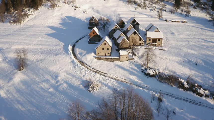 A path through the snow leading to a group of houses in snow covered clearing in the countryside during the day