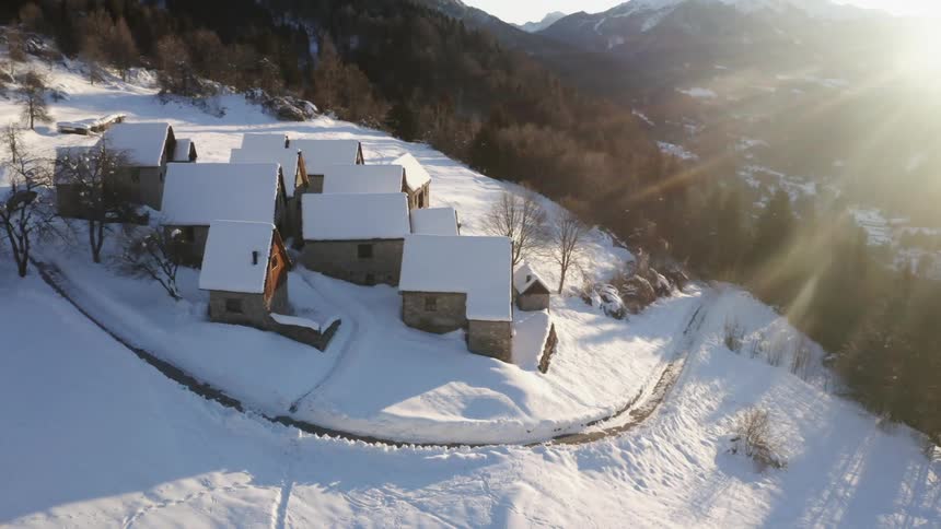 A group of small buildings on the snowy slope of a mountain on a sunny winter day
