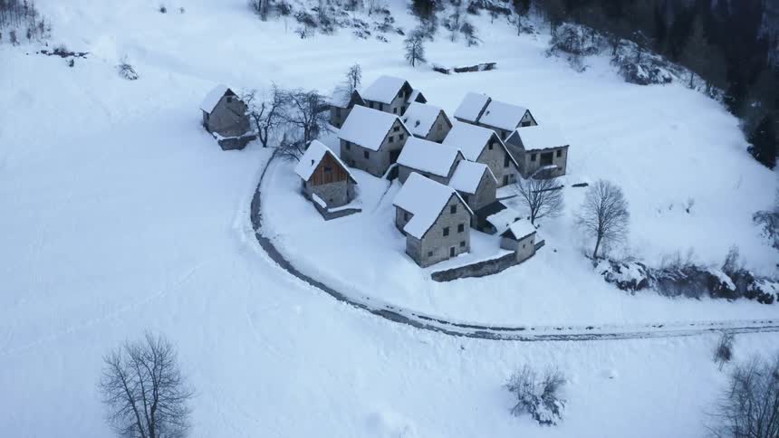 A very small cluster of buildings sit high up the side of a snow covered mountain