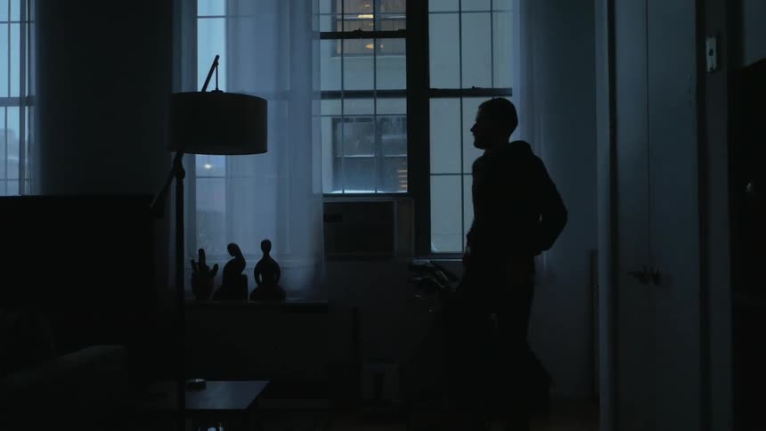 Mans silhouette stands near window holding phone to ear then turns and leaves room