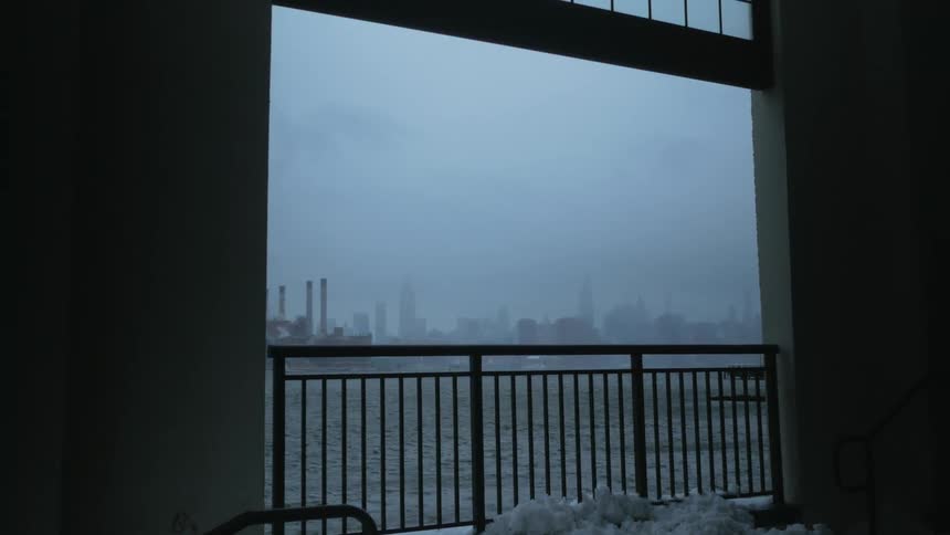 A railing and barrier across an opening showing ocean waves and a city skyline on a gray foggy day
