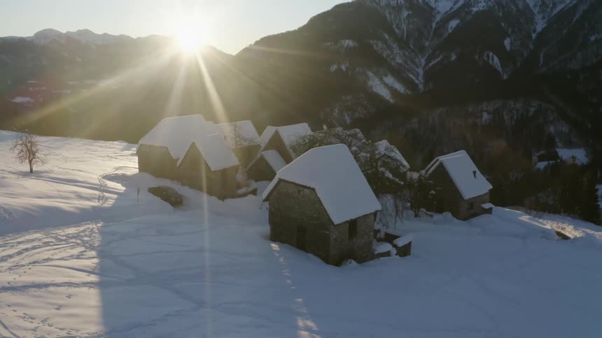 The sun shining over a small village in snowy mountains on a winter day