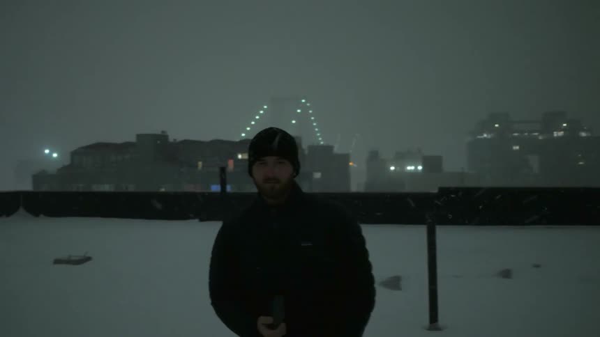 A man standing on a rooftop at night takes pictures as the snow falls