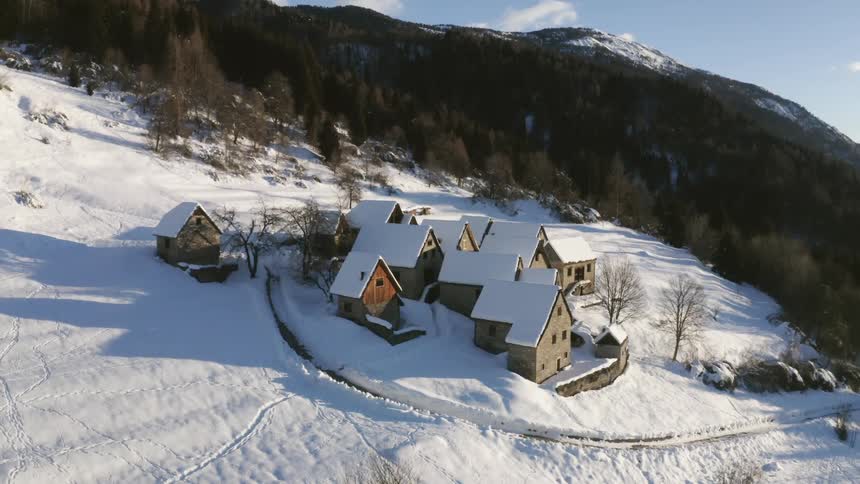 Buildings on a snow covered hill in front of a forest in a rural area