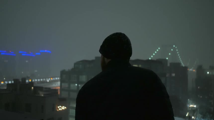 A man in a cap overlooking city buildings on a foggy night