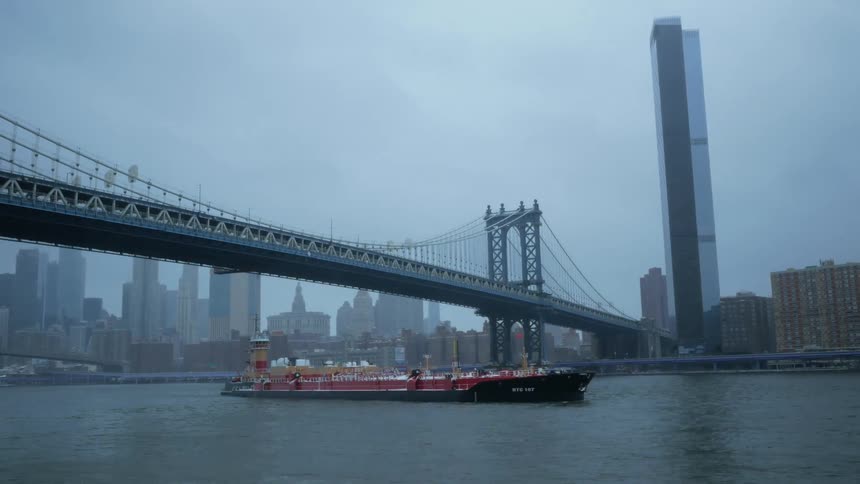 Container ship passes under suspension bridge paralleling highway with mist covered city in background