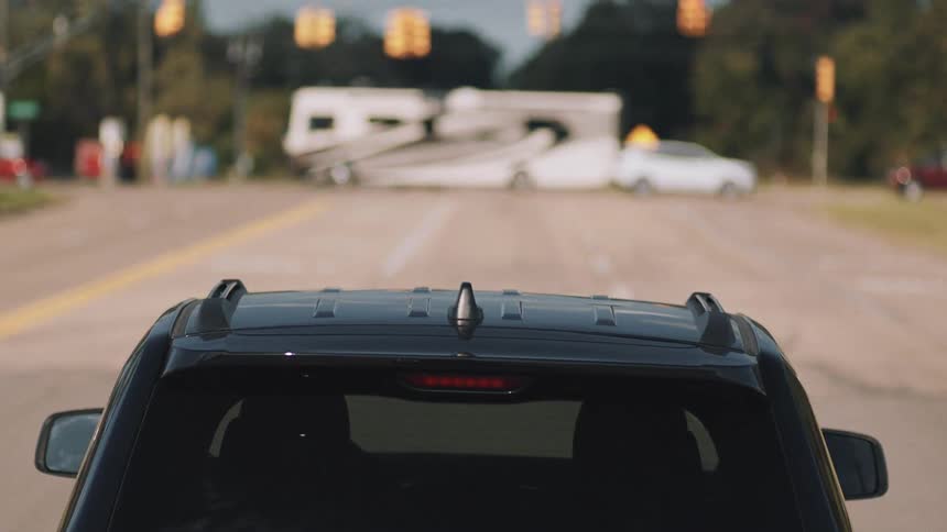 A vehicle slowly travels down a road towards a busy intersection during the day