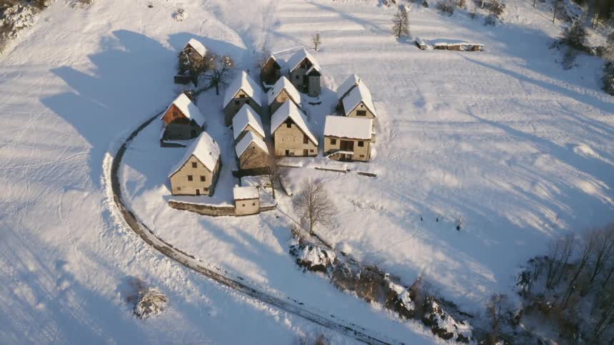 A narrow road leads to a small neighborhood covered in snow in a rural area surrounded by forest