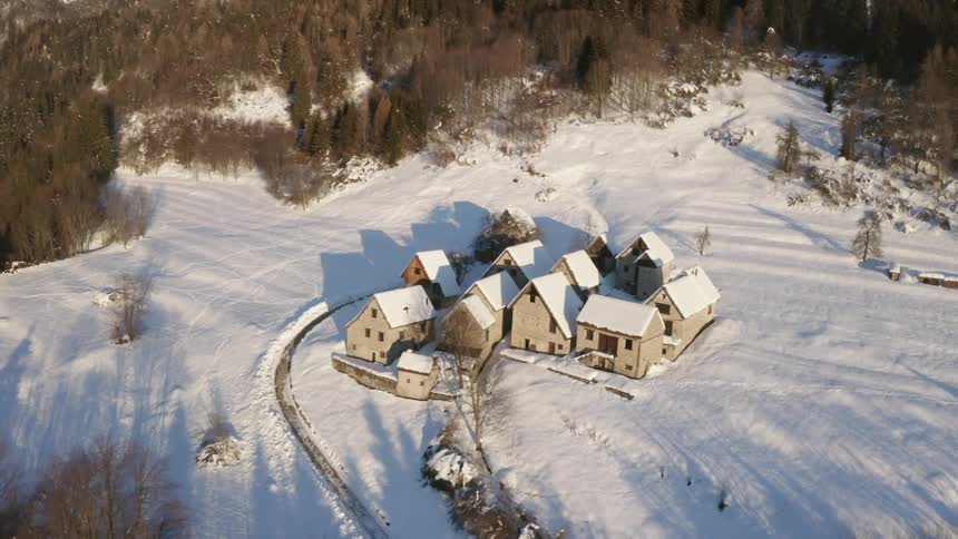 An aerial view of buildings on snow covered land by a forest in a rural area