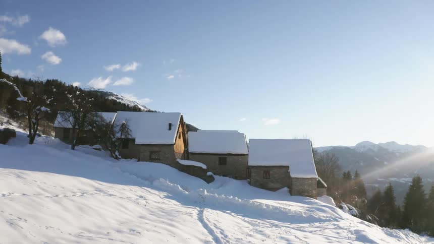 The sun shines and glares over a mountain ridge on several cabins on a snow covered slope