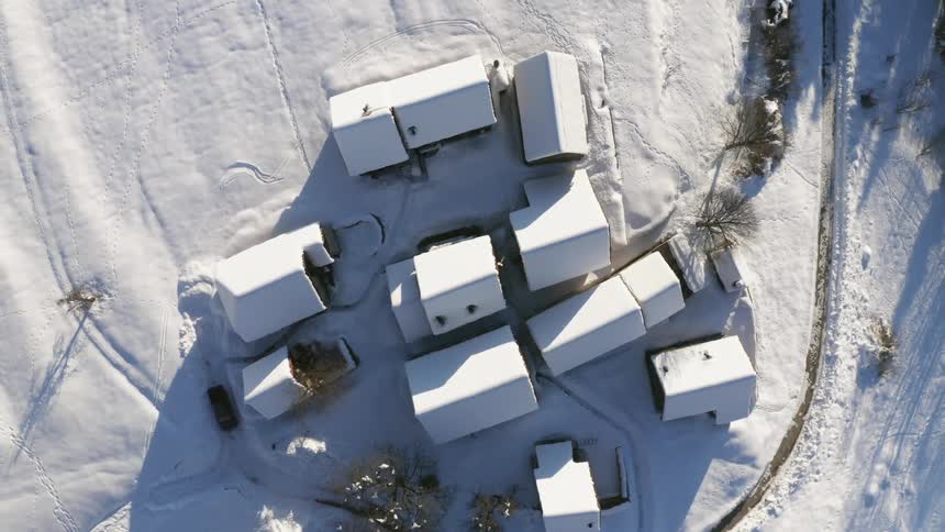 A group of snow covered one story buildings in a wintry countryside during the day