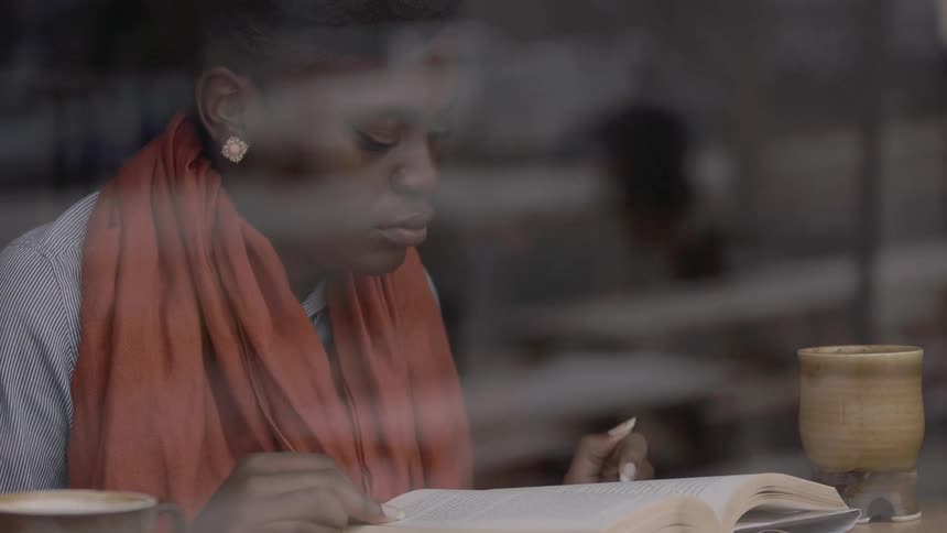 A woman sits at a table reading a book