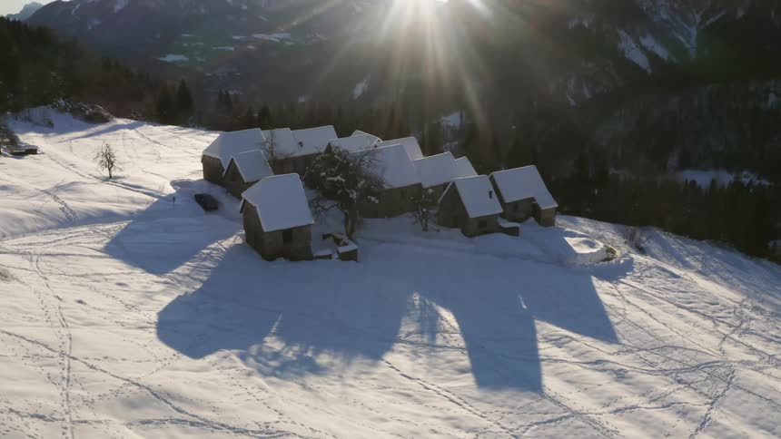 The sun shines bright over a small neighborhood covered in snow near a mountain range