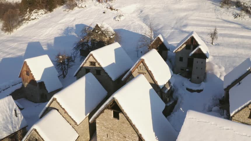 Snow covers roofs of town buildings on slope near woods