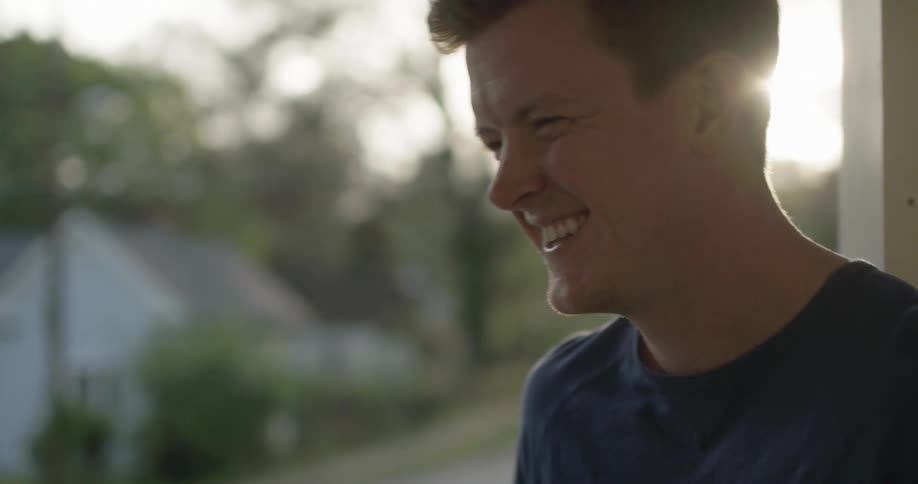 A man smiles and laughs outside on a porch