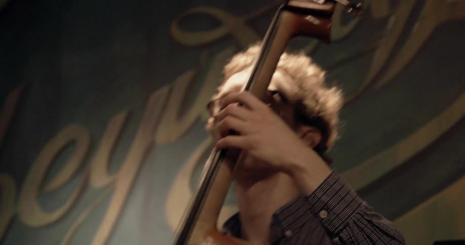 A man plays a standing bass on a stage and another man plays the drums