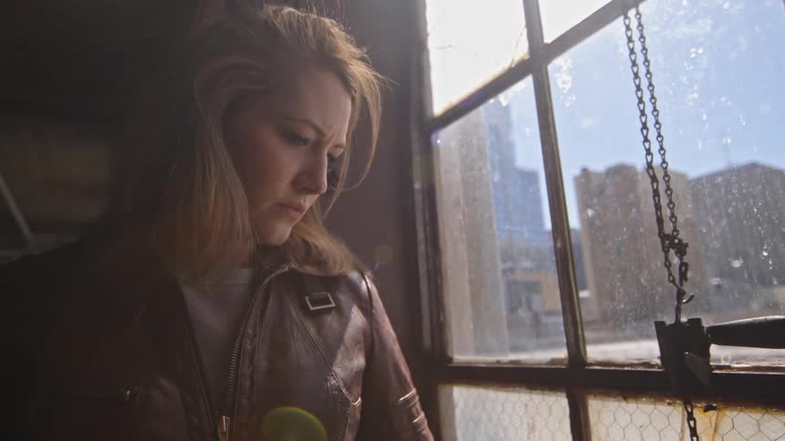 A woman looks down and out of a paned-glass window during the day in a city
