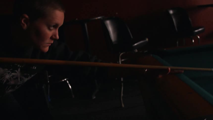 A woman is playing pool in a dark room