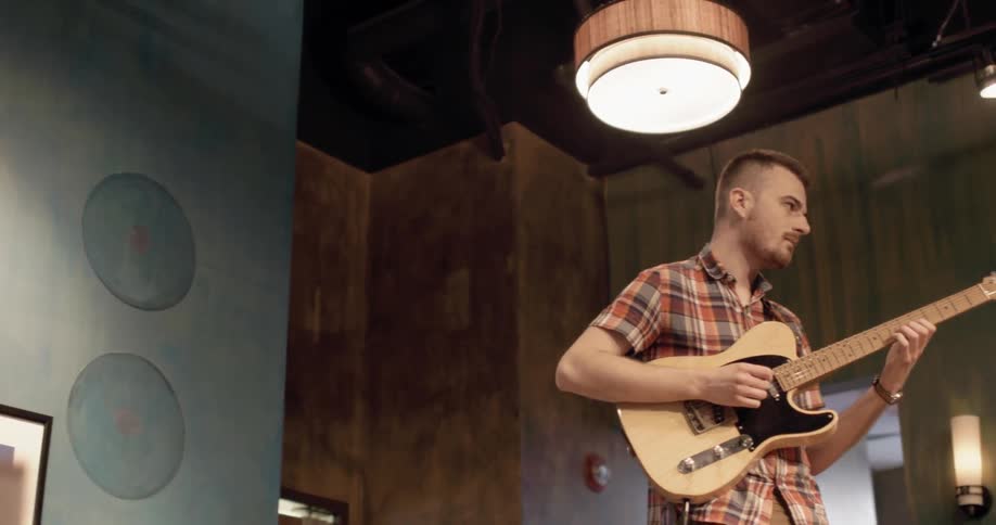 A man in a plaid shirt plays guitar under a light