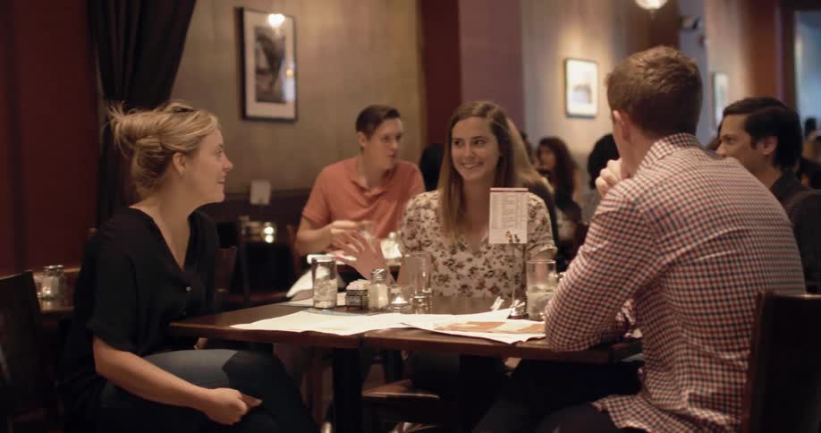 Friends sit talking at a table in a crowded restaurant