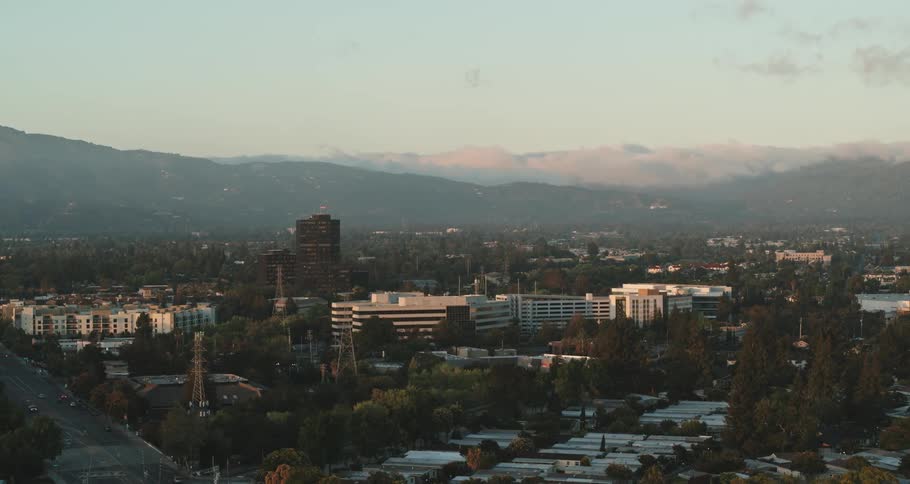 A city with buildings and trees with a mountain range the sky and clouds in the background