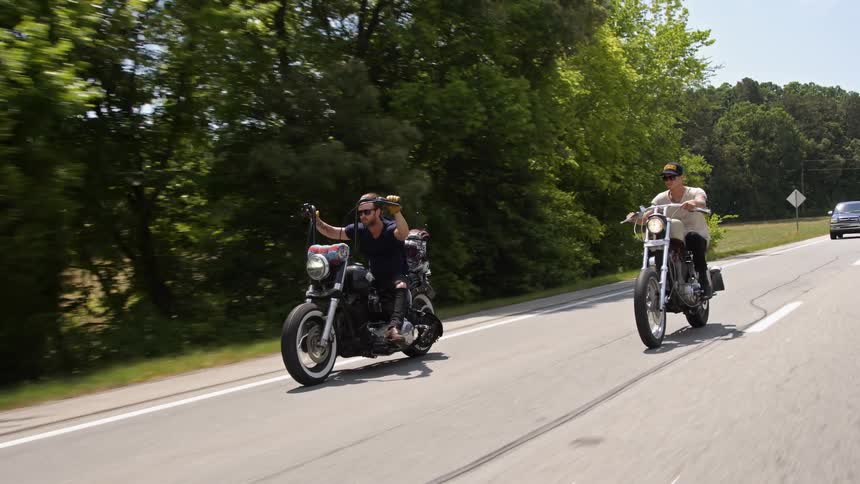 Two men riding motorcycles along a rural road