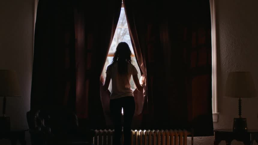 A woman opens the blinds of a window