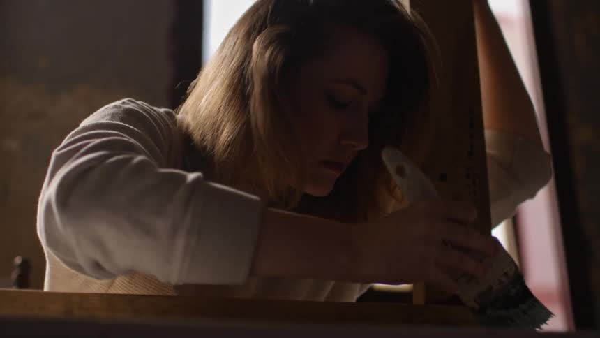 A woman is painting wood in a room