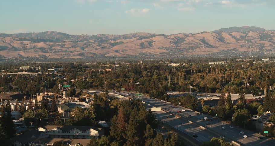 Busy highway with many buildings around and many trees and mountains in the distance