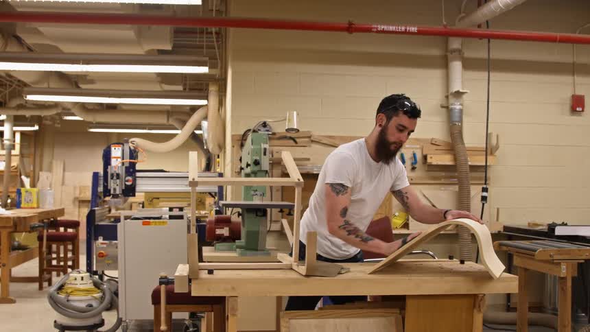 A man sands a piece of curved wood in a workshop