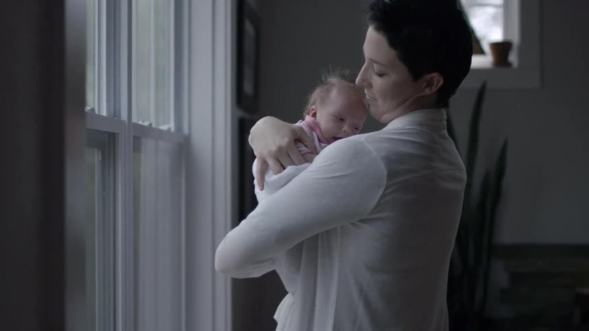 A woman holding a baby while standing near a window