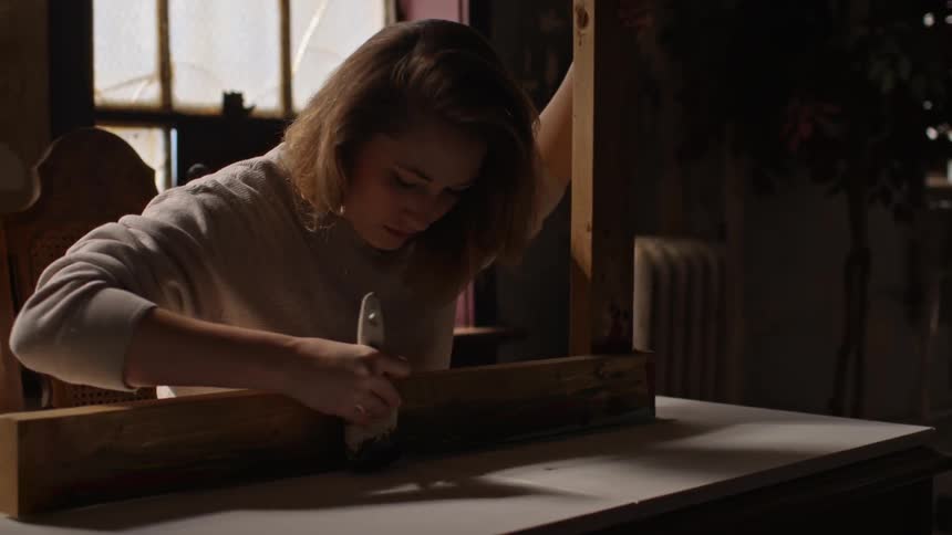 A woman using a board to paint a straight line on another surface