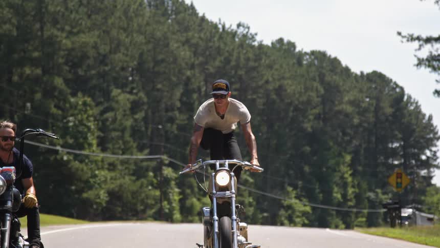 A man stands and balances on a moving motorcycle