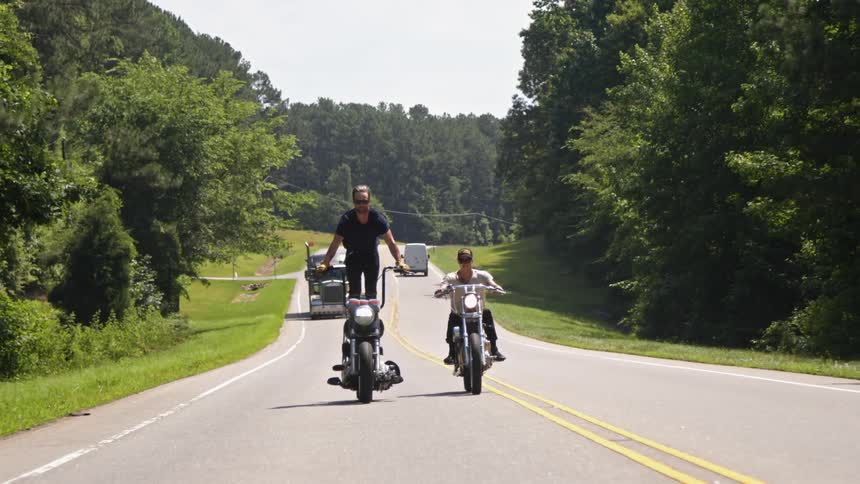 A man stands up on his motorcycle while driving down a road