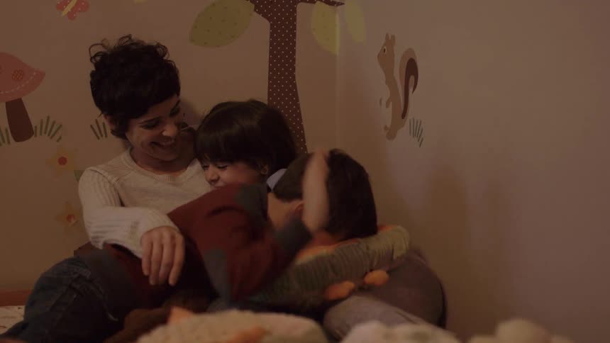 A woman and two children laughing and cuddling on a bed