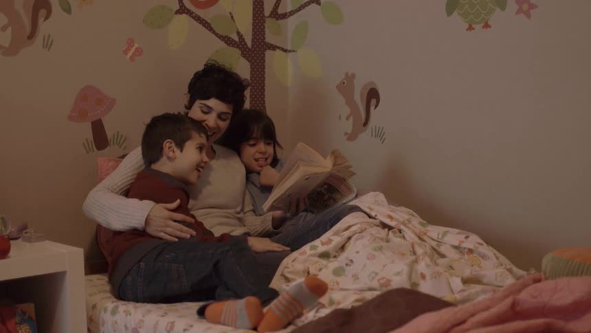 A woman is in bed reading to her children