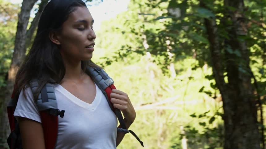 A woman with a backpack hikes along a river on a sunny day