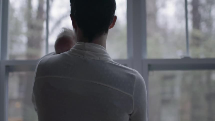 A woman holding a baby near windows