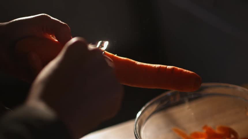 A carrot is being peeled into a bowl