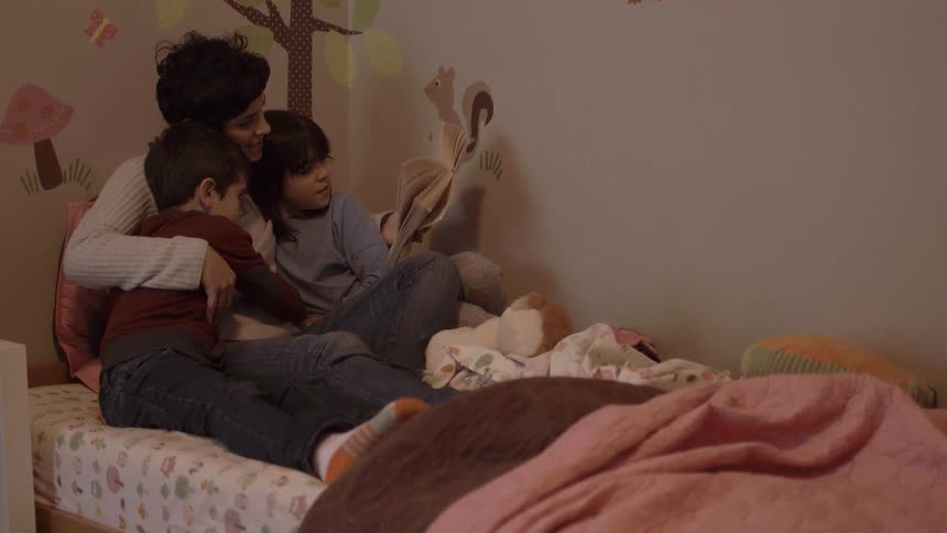A woman is on a bed reading to two children