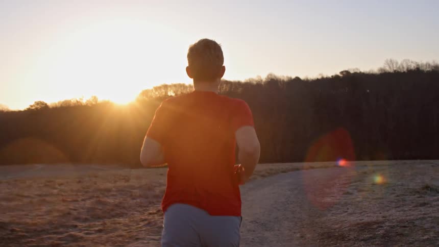 Male jogger running a trail at sunrise on a chilly day