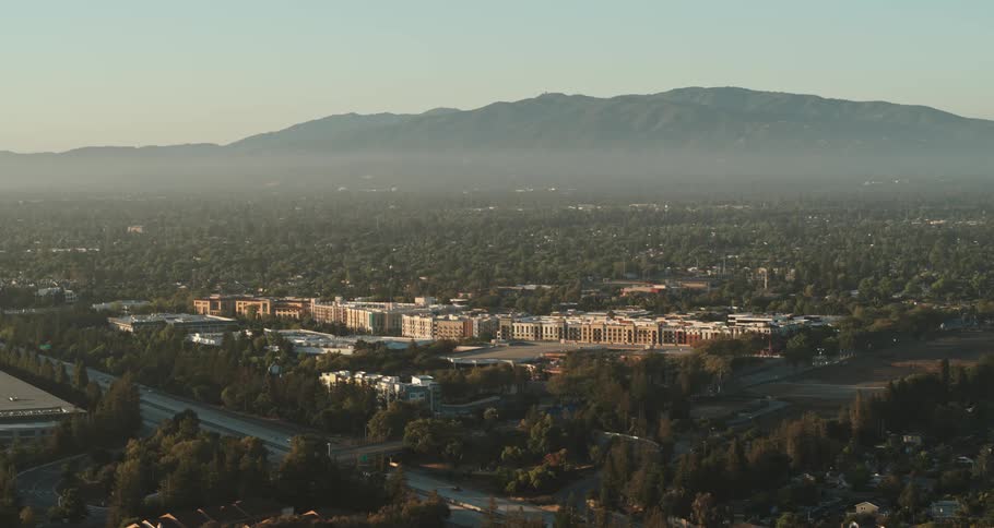 A town with buildings surrounded by trees with a mountain range the sky and clouds in the background