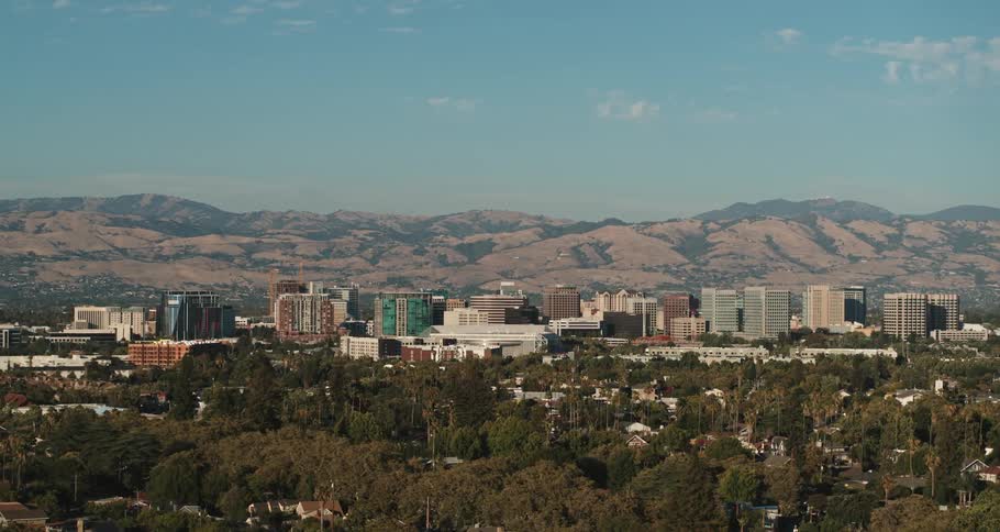 Tall city buildings with many trees in front and mountains in the distance