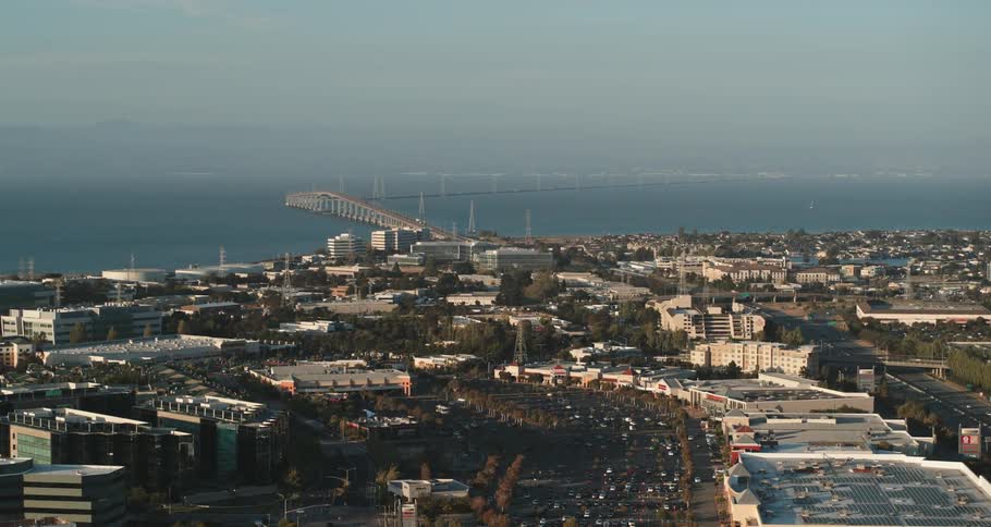 A coastal city with buildings and trees with a bridge the ocean sky and clouds in the background